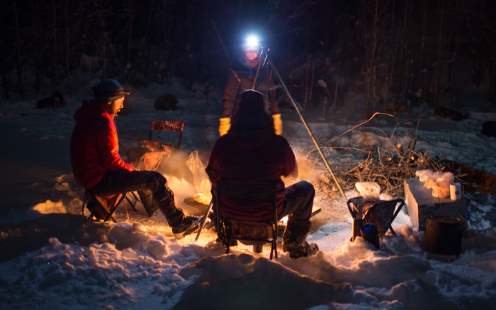 a group of people sit around a campfire in the snow